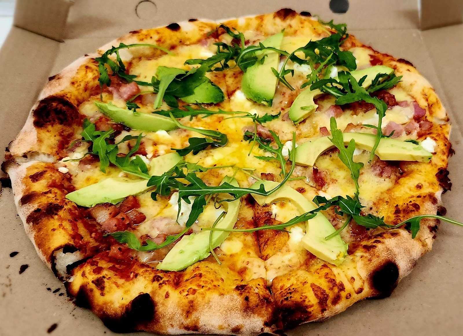 Pizza topped with avocado, rocket and bacon in a box