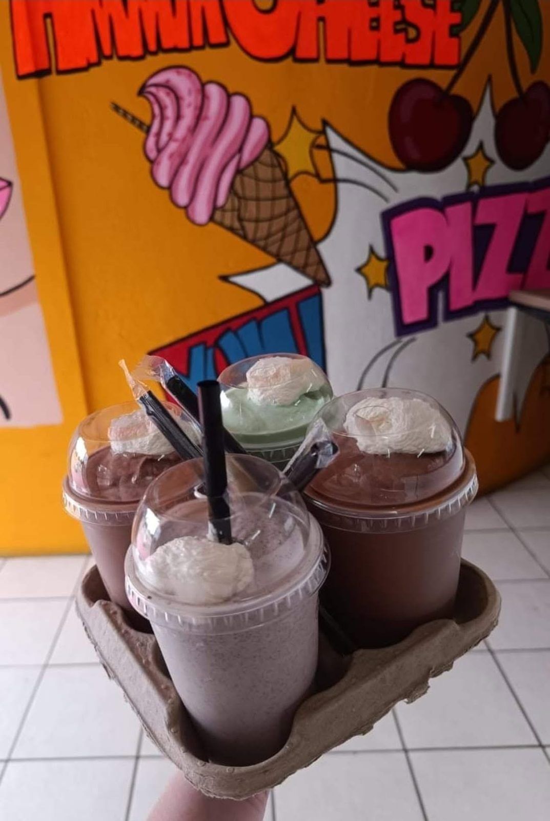 Four milkshakes in a carry tray in front of the shop mural